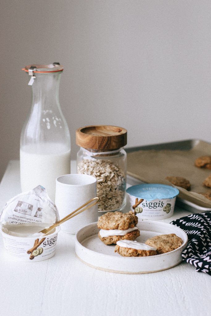 Oatmeal cookie sandwiches with yogurt filling on a white plate with jug of milk and yogurt containers 