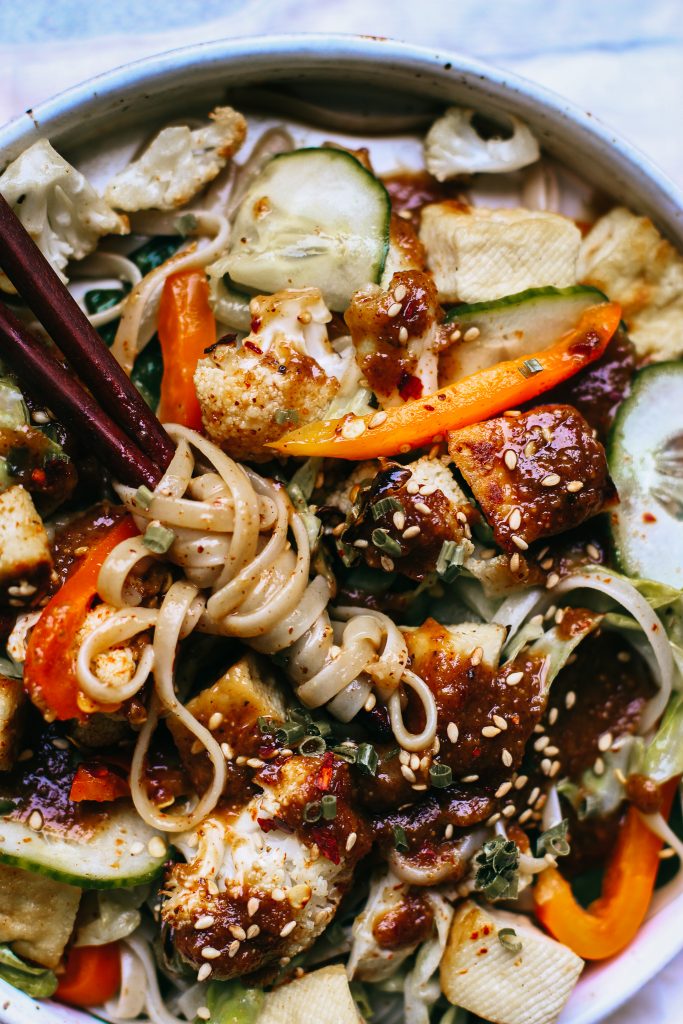 Noodles wrapped on chopsticks with veggies and tofu in a white bowl