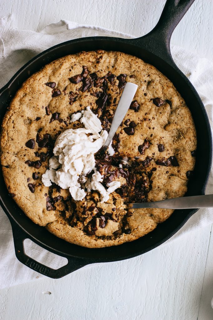 chocolate chip cookie skillet topped with ice cream in a cast iron pan with two spoons
