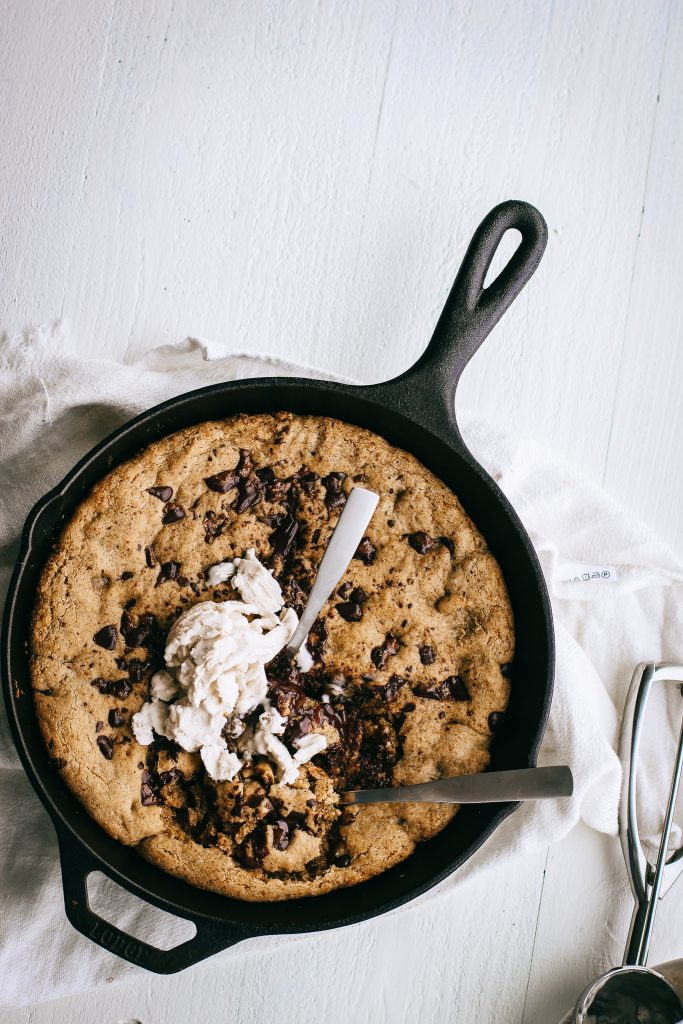 chocolate chip cookie skillet topped with ice cream in a cast iron pan with two spoons