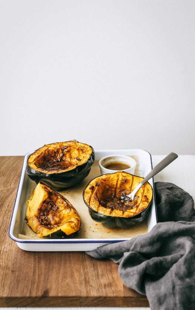 Acorn squash with melty brown butter on a white tray with a spoon