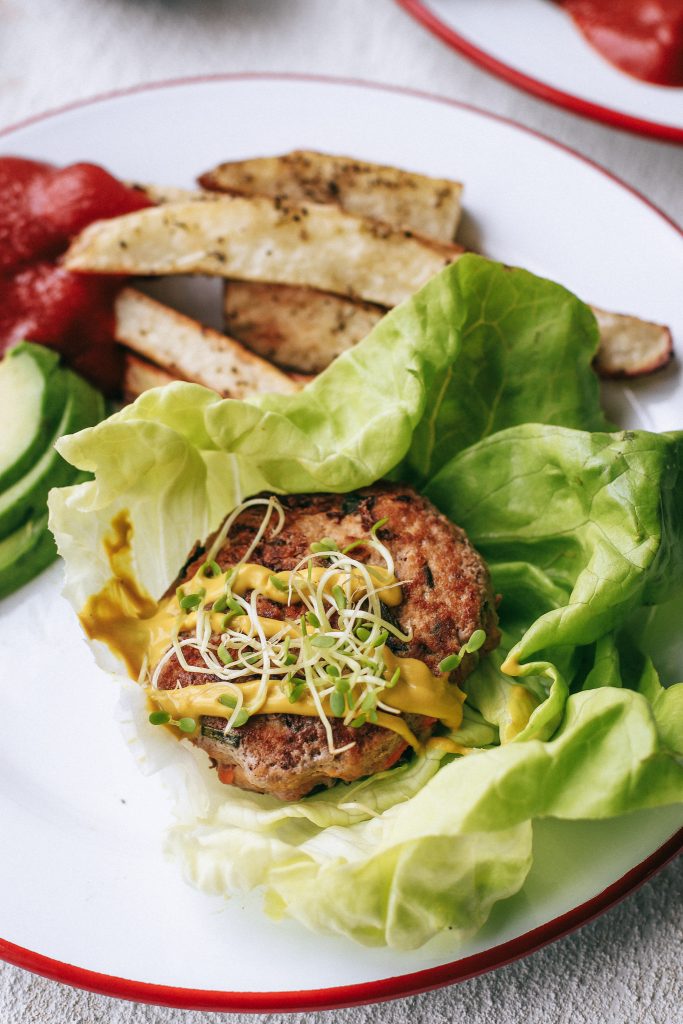Up close picture of a buffalo turkey burger with mustard and micro greens in a lettuce wrap on a plate. 