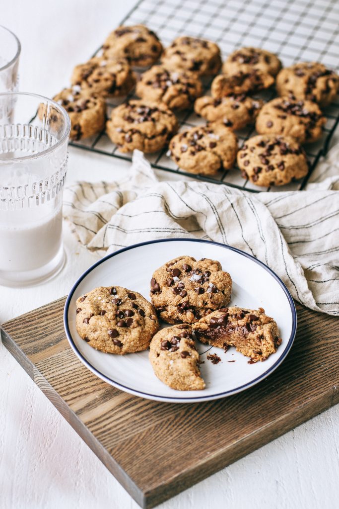 Chocolate chip cookies on a blue and white plate with a glass of milk and cookies on a cooling rack