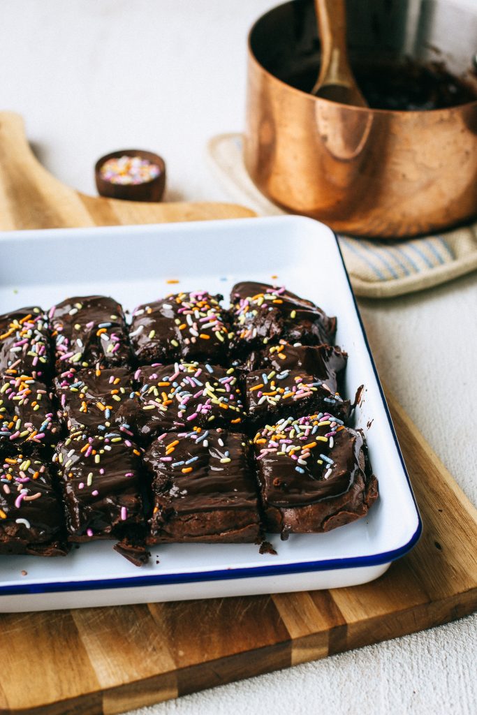 chocolate brownies with sprinkles on a white tray and wood cutting board with a pot of melted chocolate