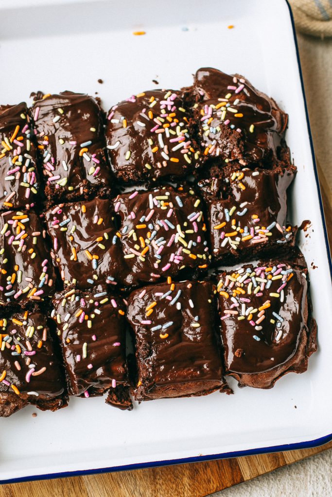 chocolate brownies with sprinkles on a white tray and wood cutting board with a pot of melted chocolate
