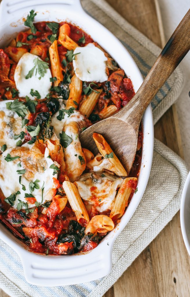 baked pasta with spinach and cheese in a white dish with a wooden spoon