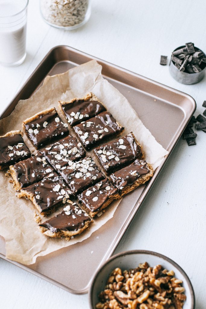 walnut oat cookie squares topped with melted chocolate on a baking tray with parchment paper