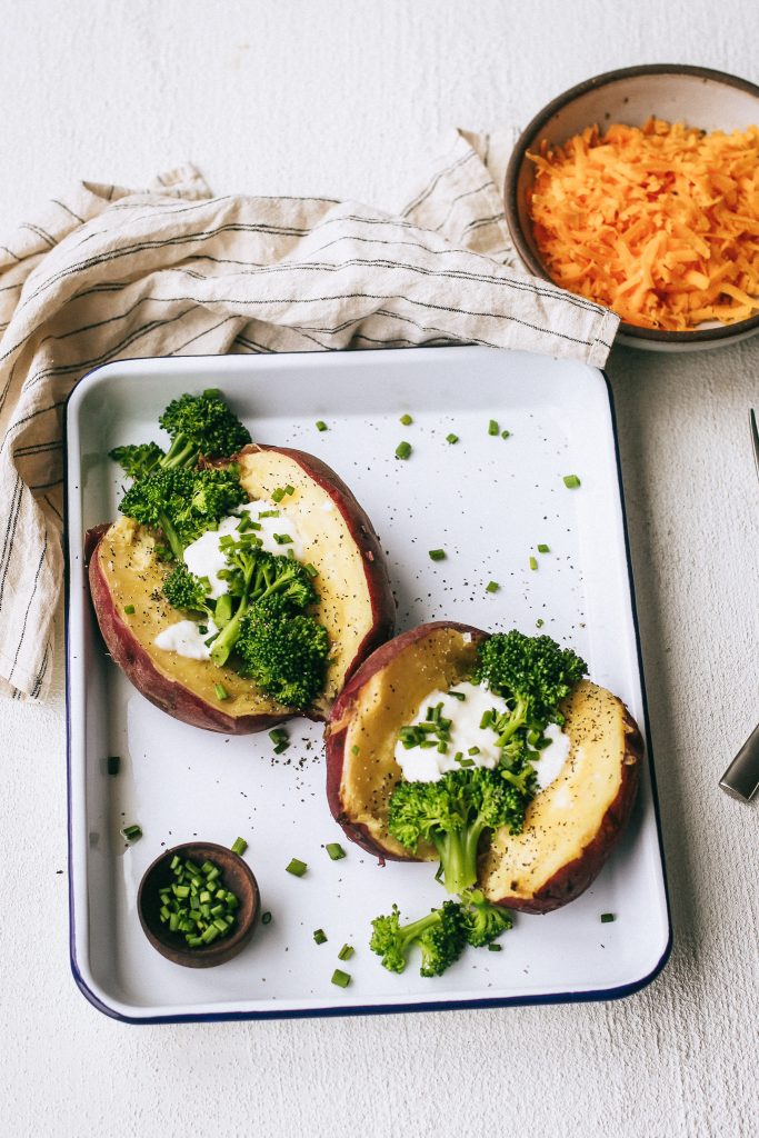 baked potato with broccoli and chives on a white tray with a bowl of cheese