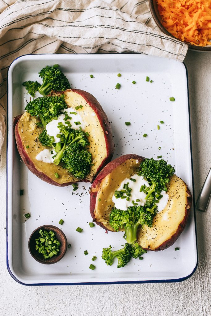 baked potato with broccoli and chives on a white tray with a bowl of cheese