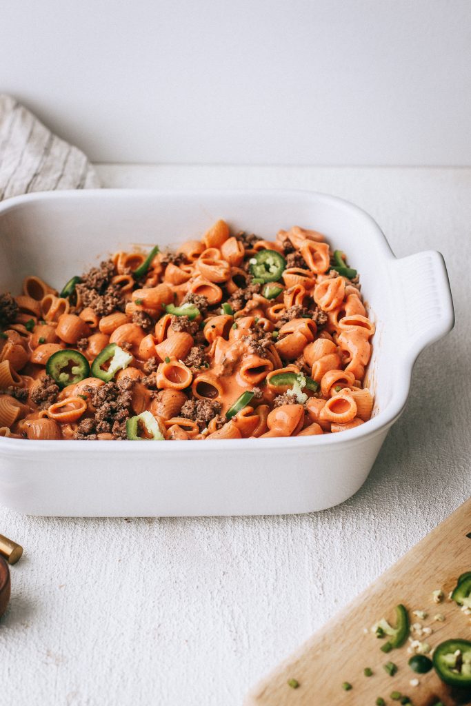 taco pasta in a white casserole dish with jalapeños on cutting board