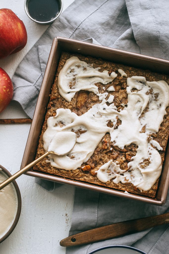 baked apple oatmeal in baking dish with cashew frosting and a gold spoon