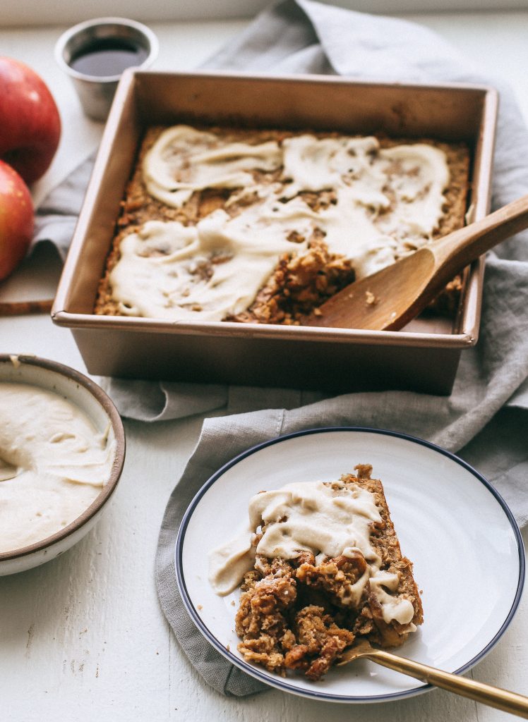 baked apple oatmeal in baking dish with cashew frosting and a slice of baked oatmeal on a white plate