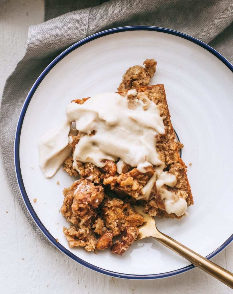 slice of baked oatmeal with cashew frosting on white plate with grey dish towel