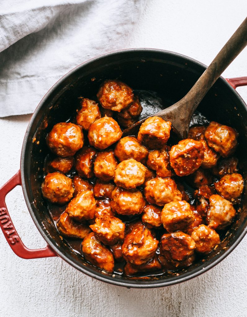 cocktail meatballs in a black and red pot with a wooden spoon