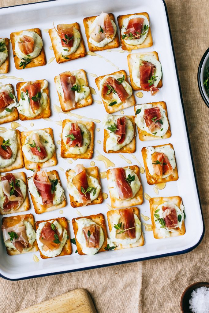 prosciutto and ricotta on crackers with honey drizzle on white tray on table cloth