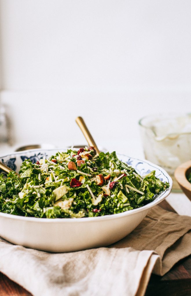 kale salad in a blue and white bowl with gold spoons