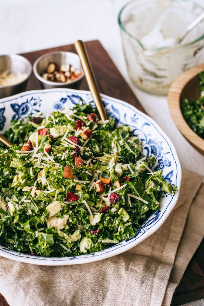 kale salad in a blue and white bowl with gold spoons