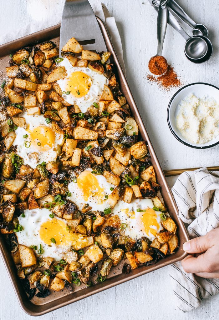potatoes brussels sprouts and eggs in a baking tray with teaspoons and dish of parmesan