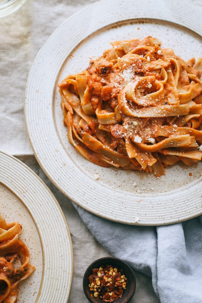 vodka sauce pasta on pale yellow plate with small dish of red pepper flakes