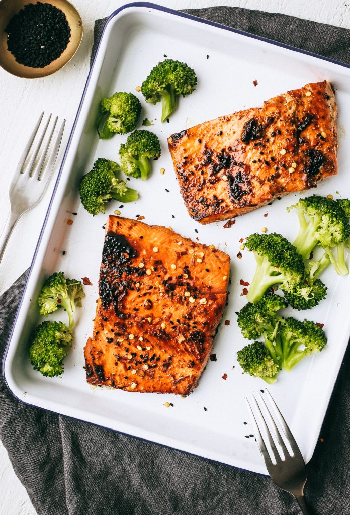 salmon and broccoli on white tray with fork and small bowl of black sesame seeds