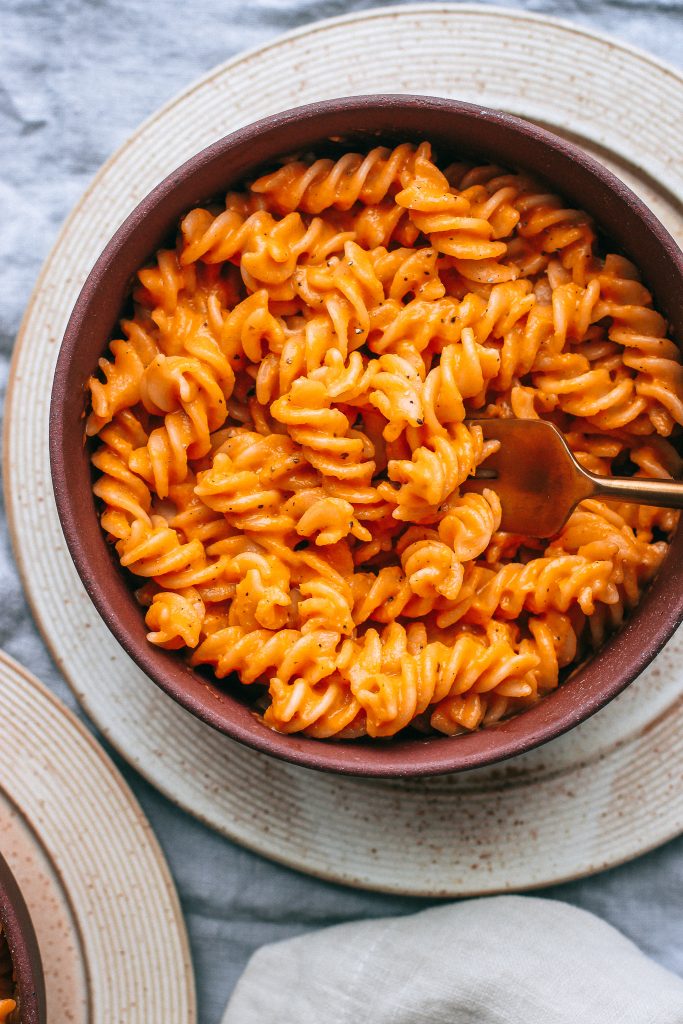 red pepper pasta in a maroon bowl with gold fork