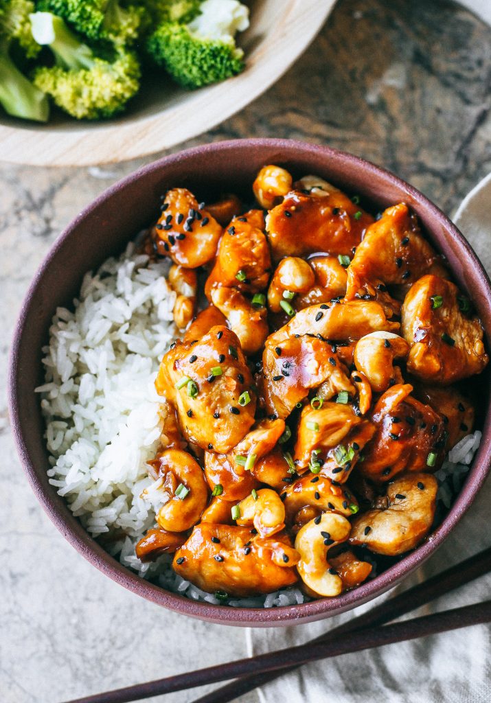 orange cashew chicken with white rice in a maroon bowl