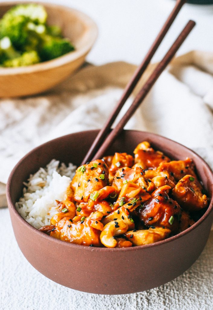 orange cashew chicken with white rice in a maroon bowl with chopsticks