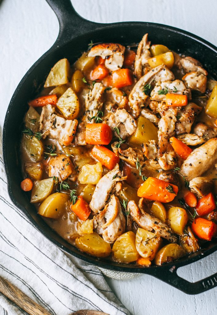 chicken, potatoes, and carrots in a creamy white wine sauce in black skillet