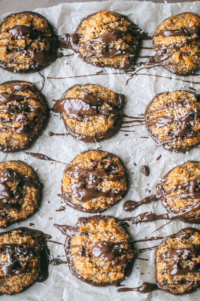 samoa cookies topped with melted chocolate and shredded coconut on parchment paper