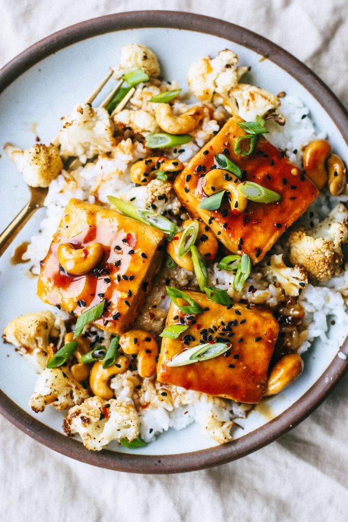 orange cashew tofu with rice and cauliflower on a plate