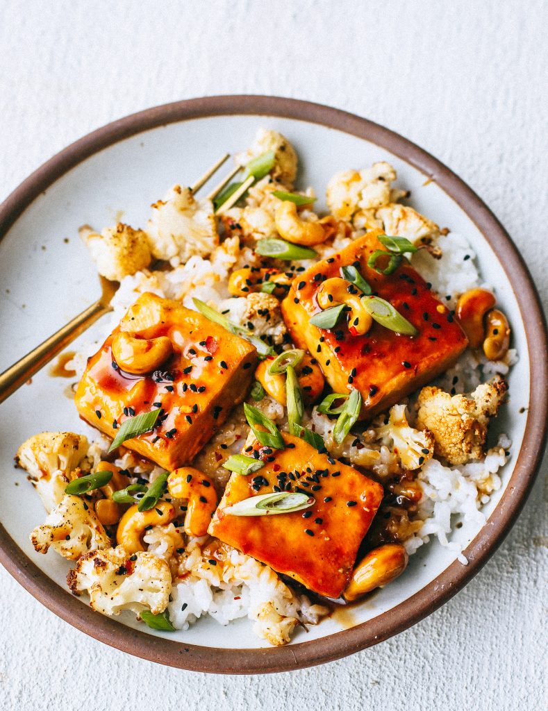 orange cashew tofu with rice and cauliflower on a plate