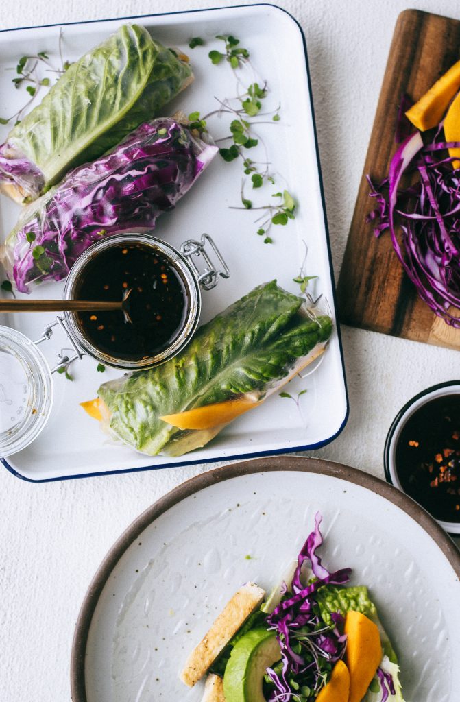 spring rolls with mango, purple cabbage, and lettuce on a white tray with sweet chili dip 