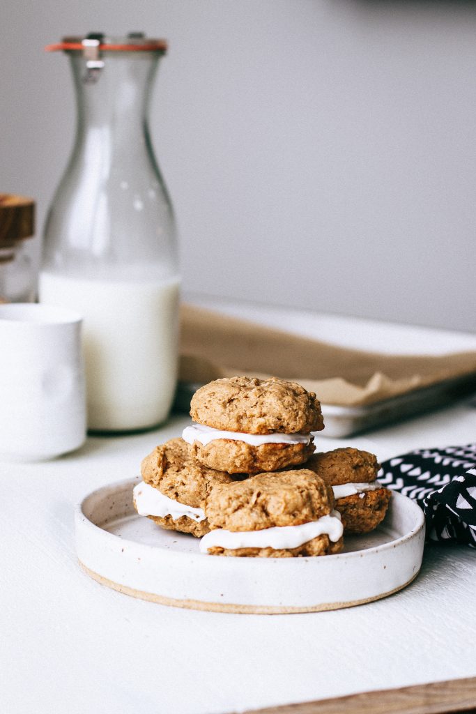 oatmeal yogurt cookie sandwiches stacked on plate with jar of milk