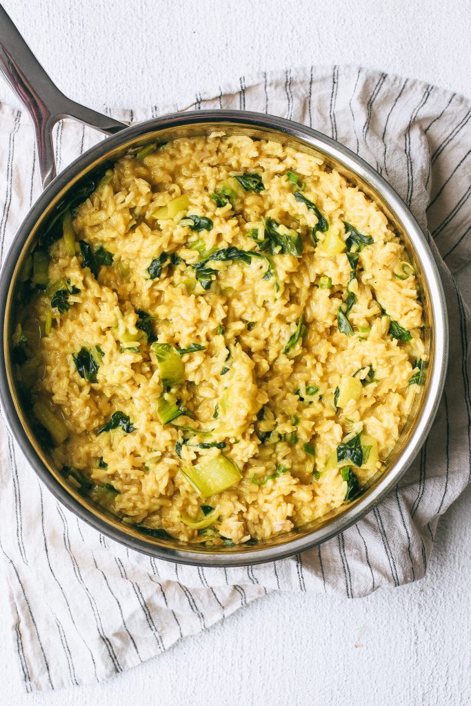 creamy yellow rice with bok choy and spinach in a pan on a dish towel
