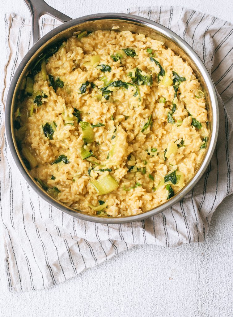 creamy yellow rice with bok choy and spinach in a pan on a dish towel
