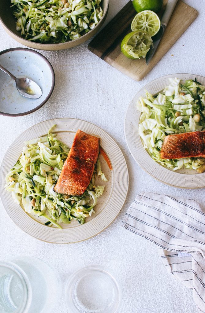 cabbage and cucumber salad with salmon on plates and limes on wood cutting board