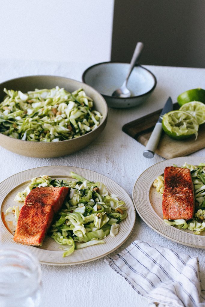 gluten free cabbage and cucumber salad with salmon on plates and limes on wood cutting board