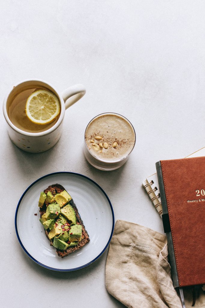 salted caramel smoothie topped with peanuts, avocado toast on plate, lemon water, daily planner