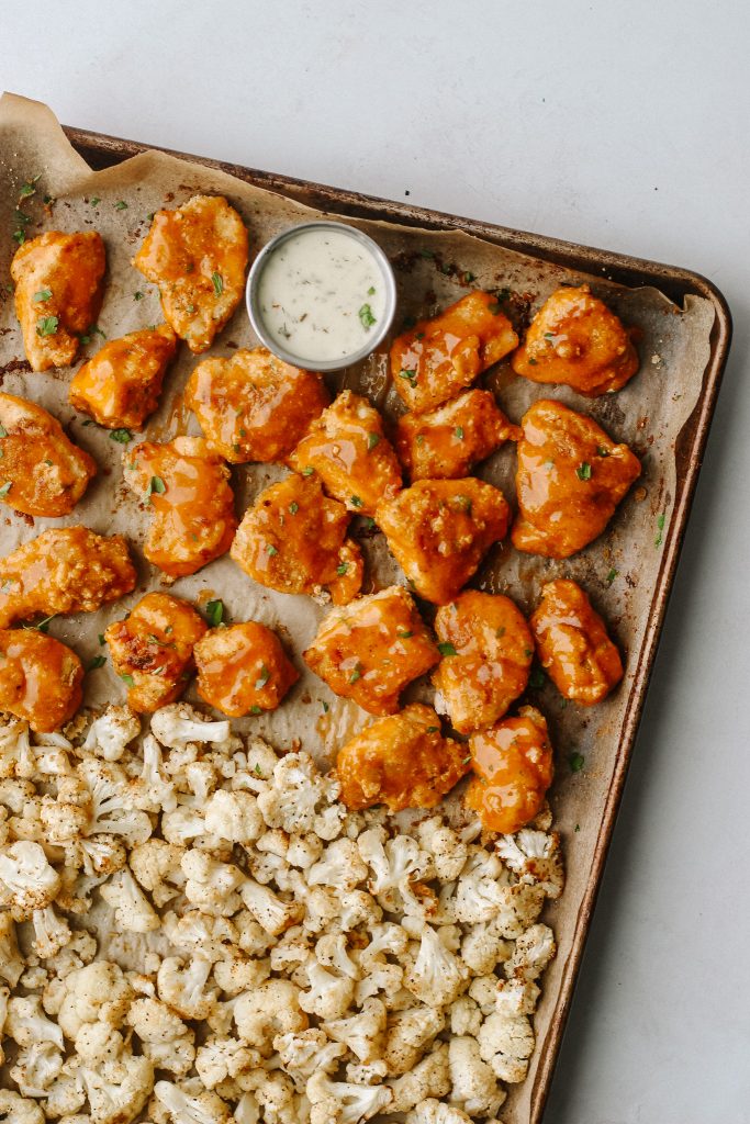 buffalo chicken and cauliflower on a sheet pan with a bowl of ranch