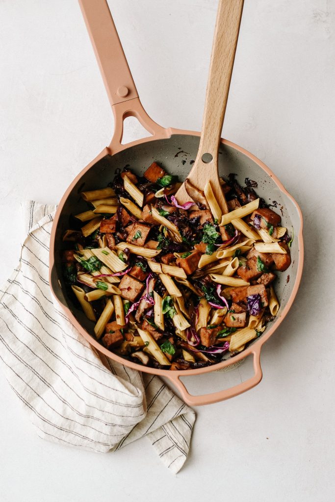 penne noodles, cabbage, mushrooms, tofu, and spinach stir fry in frying pan with wooden spoon