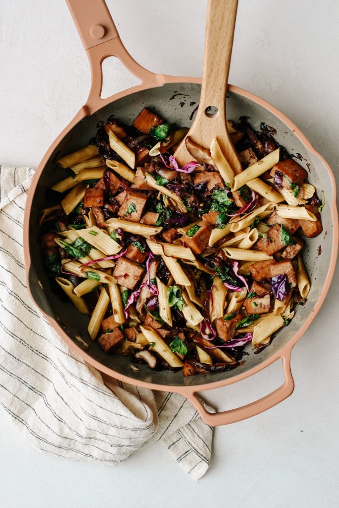 penne noodles, cabbage, mushrooms, tofu, and spinach stir fry in frying pan with wooden spoon