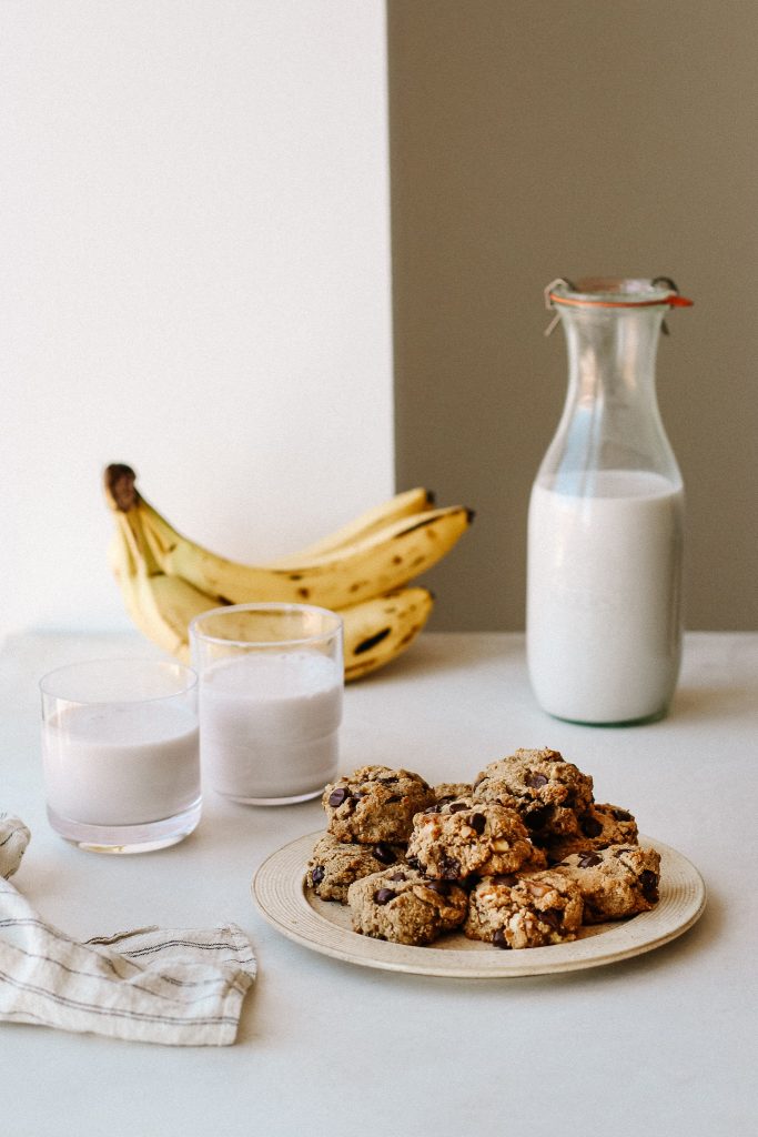 banana cookies on a plate with glasses of milk, jar of milk, and bananas 