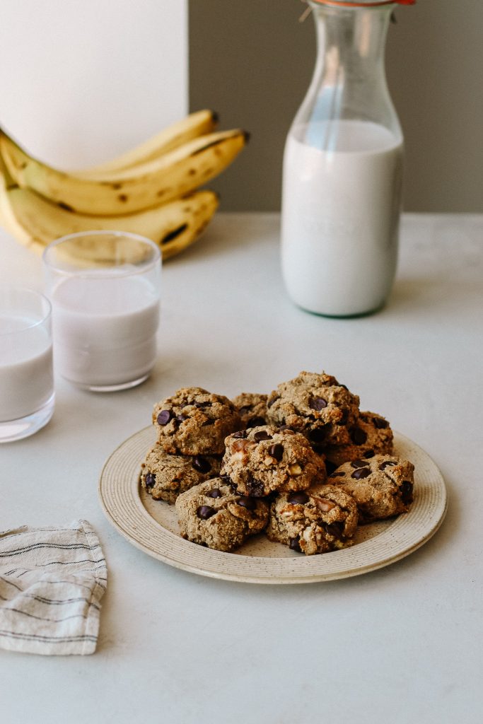 banana cookies on a plate with glasses of milk, jar of milk, and bananas 