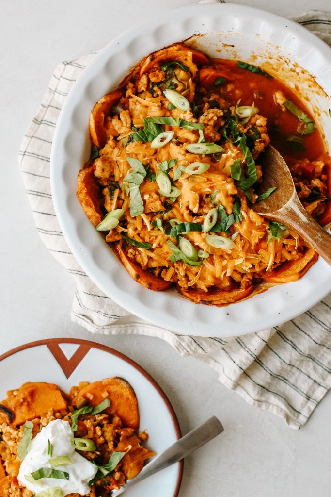 enchilada sweet potato casserole in a baking dish with wood spoon and on a plate with sour cream 