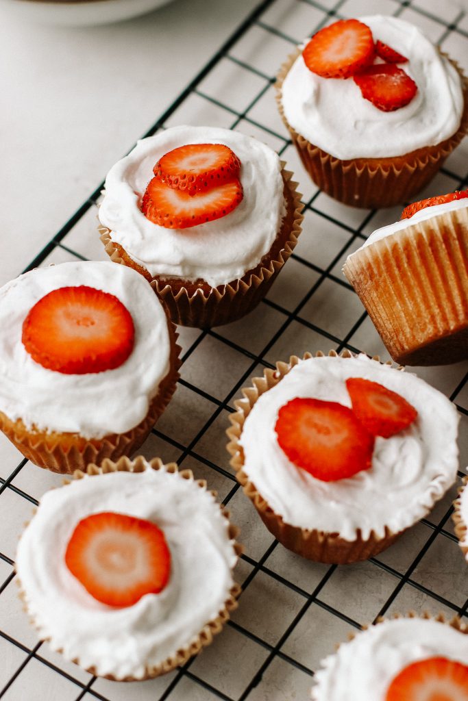 strawberry shortcake cupcakes on a cooling rack with a bowl of strawberries and bowl of cool whip
