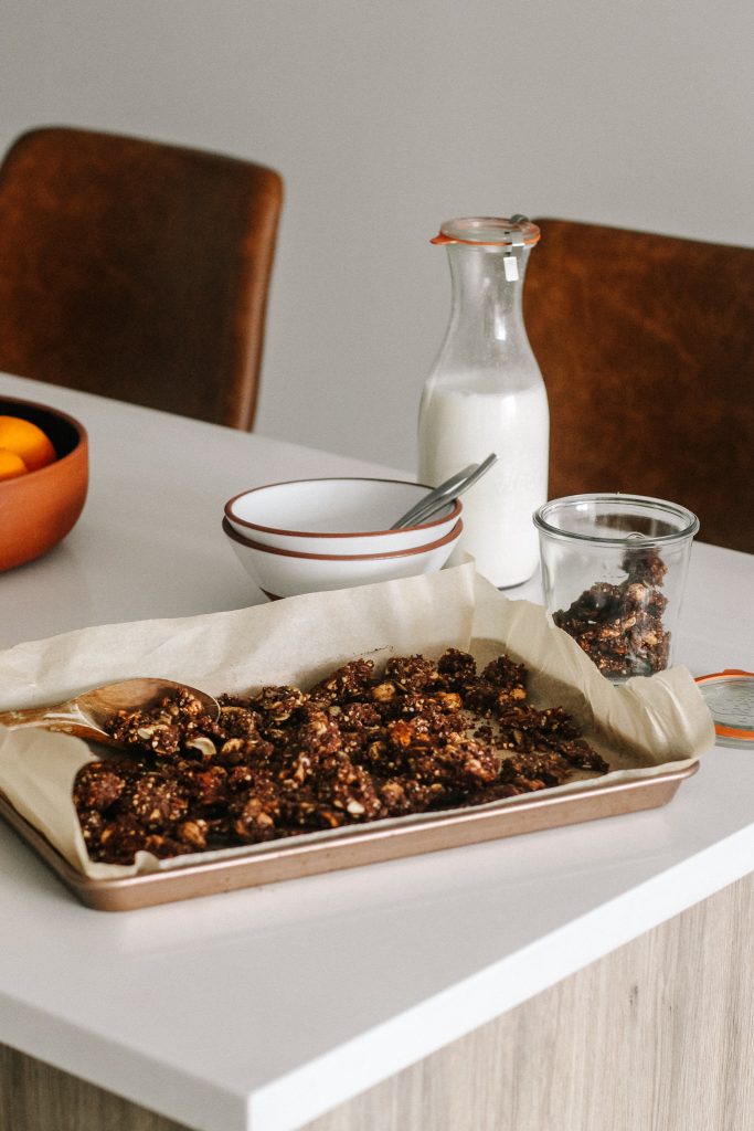 chocolate granola clusters on a baking sheet with jug of milk and bowls