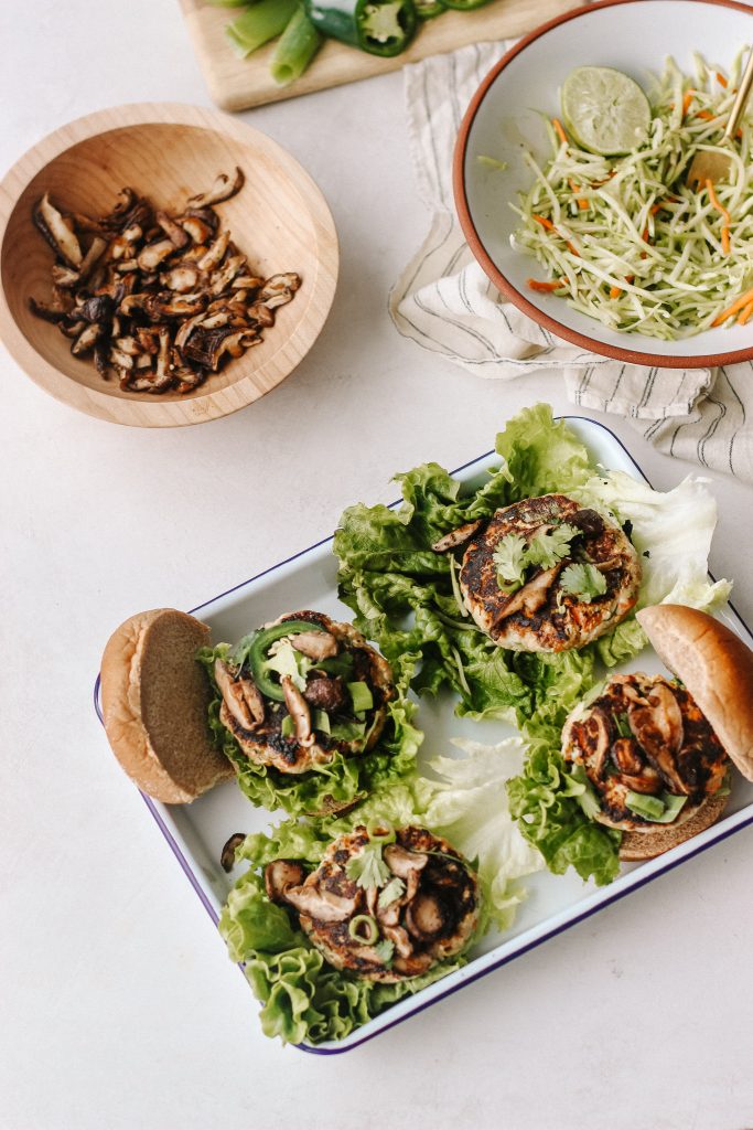 stiry fry burgers on buns and lettuce wraps on a white tray with bowl of mushrooms and bowl of broccoli slaw and jalapeno on a cutting board