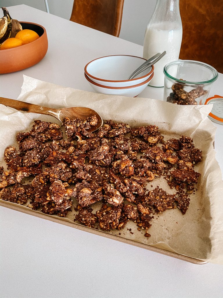 chocolate granola clusters on a baking sheet with jug of milk and bowls