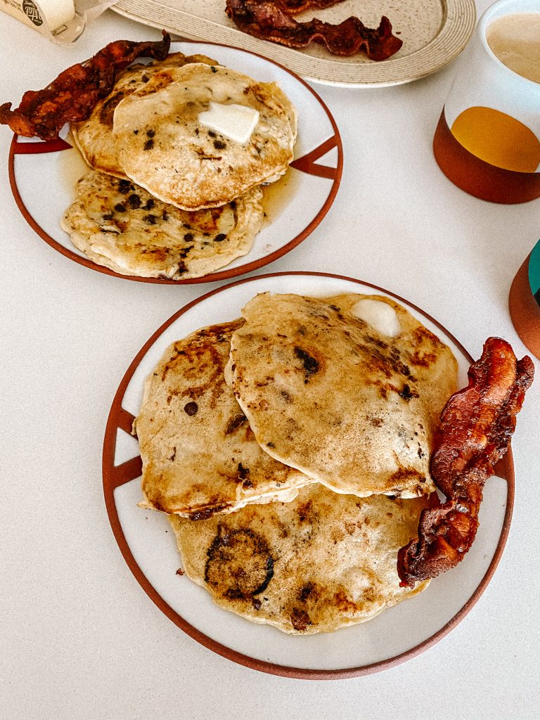 pancakes and bacon on a plate with coffee mugs