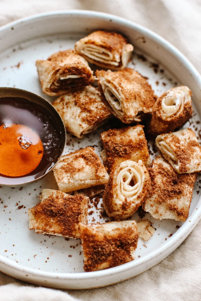 cinnamon sugar cream cheese tortilla roll ups on a plate with bowl of maple syrup